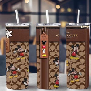 May include: Three brown Coach tumblers with white straws. Each tumbler features a repeating pattern and a Mickey Mouse design. One tumbler has a Disney tag. The Coach logo is visible on each tumbler.
