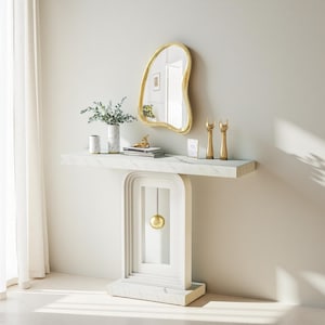May include: A white marble console table with a gold-framed mirror and decorative items. The table features a unique arched design with a gold sphere accent. A vase with greenery, books, and gold sculptures adorn the tabletop.