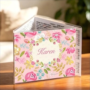 Könnte beinhalten: Ein personalisierter Acryl-Fotoblock mit floralem Design. Der Block zeigt den Namen "Karen" in eleganter Schrift in einem floralen Kranz. Der Hintergrund ist ein zartes Rosa, und die Blumen sind in Rosa-, Gelb- und Blautönen gehalten.