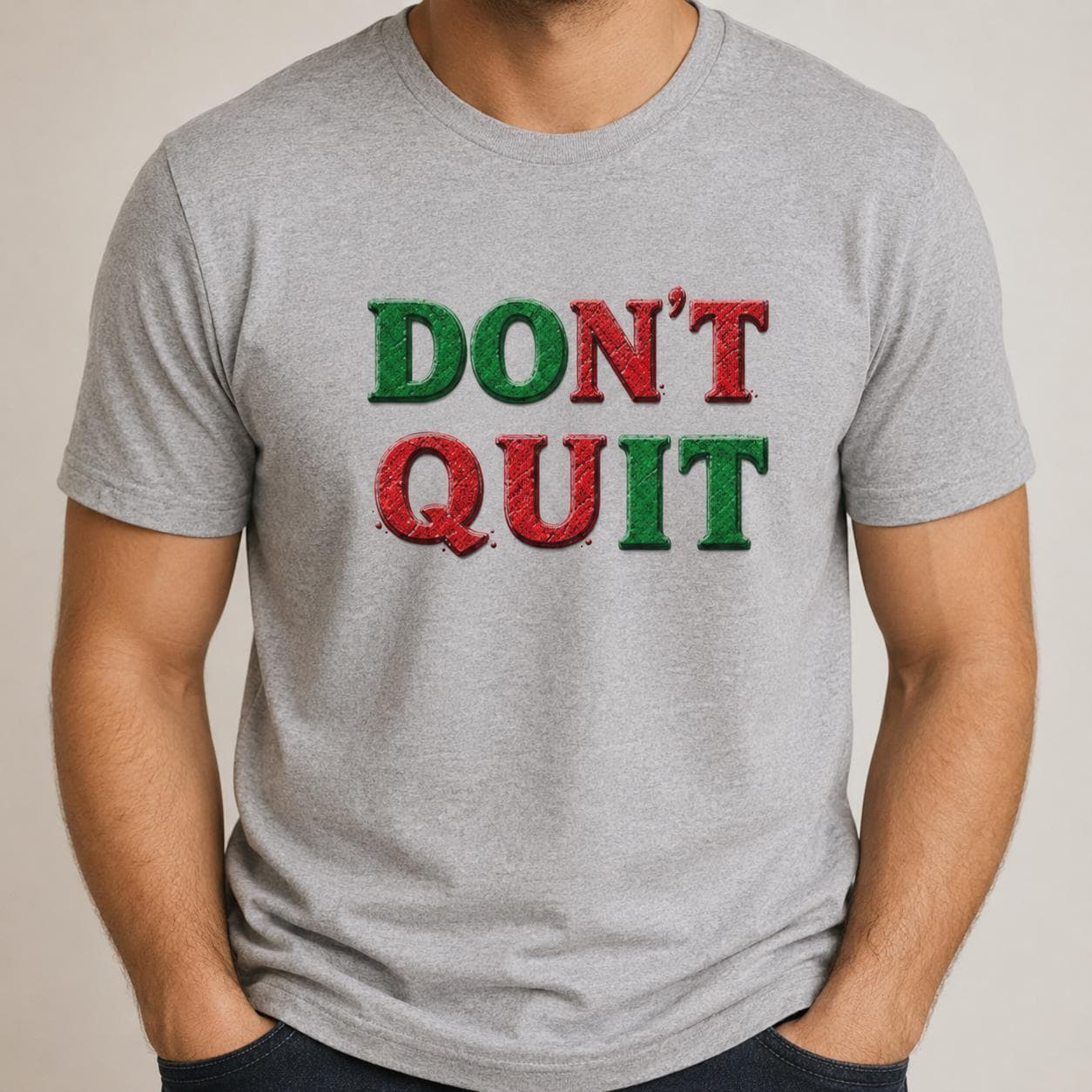 Graues T-Shirt mit ‚DON’T QUIT‘ Schriftzug in Rot und Grün getragen von Person