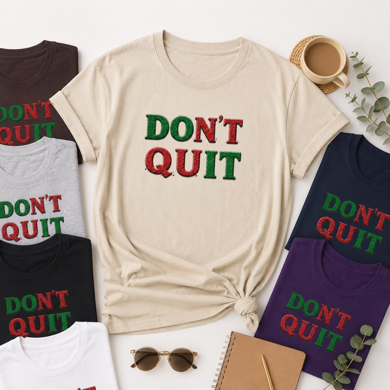 Beige und dunkelblaue T-Shirts mit ‚DON’T QUIT‘ Schriftzug liegen nebeneinander auf Tisch