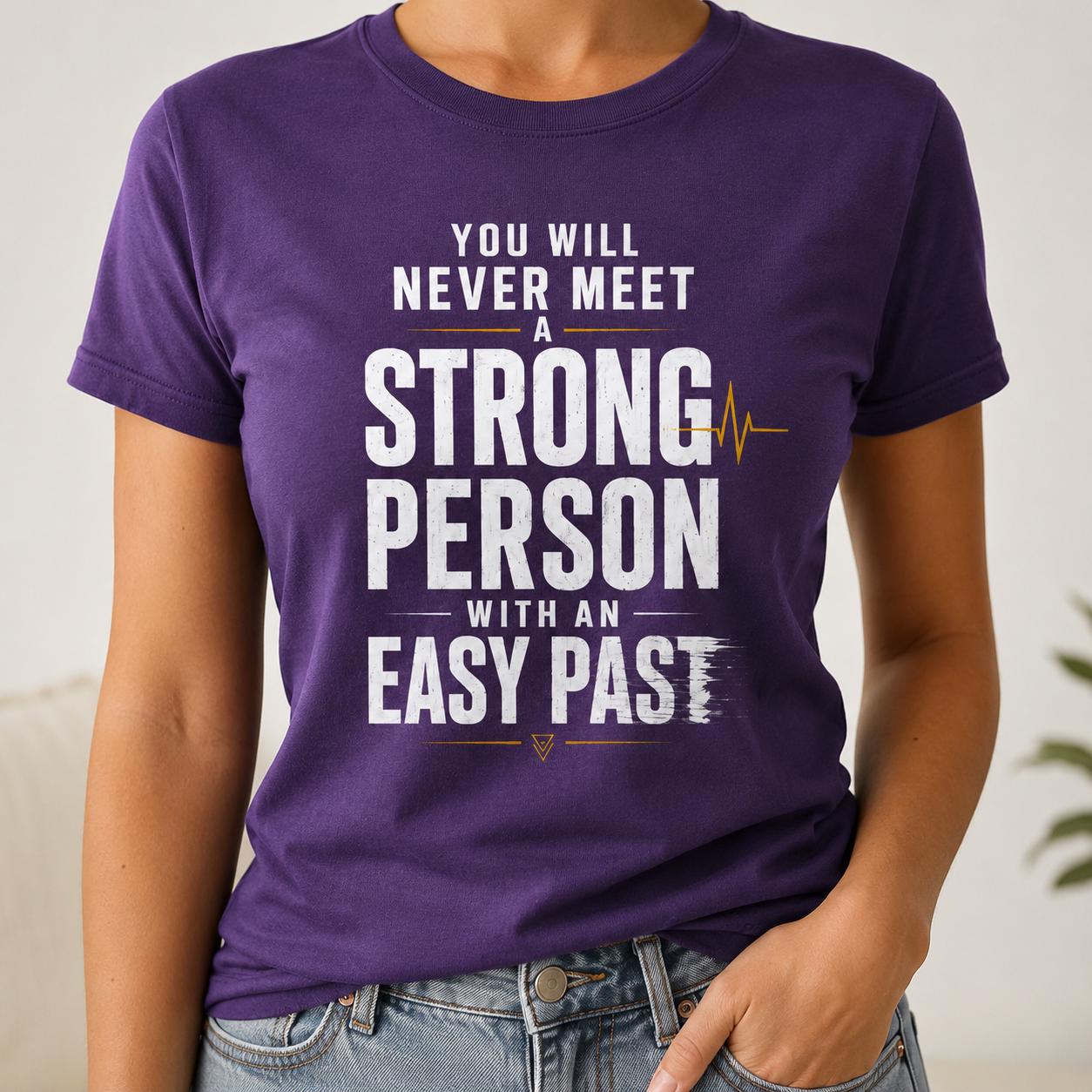 Lila T-Shirt mit weißem und goldfarbenem Schriftzug 'You Will Never Meet A Strong Person With An Easy Past' auf einer Person
