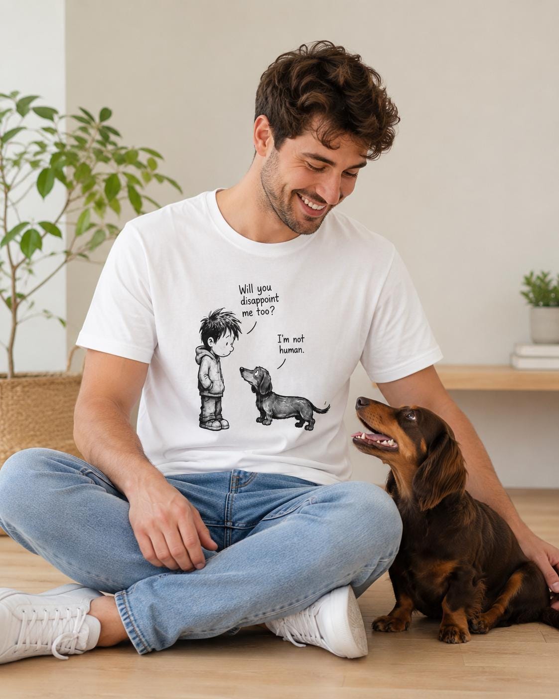 Mann sitzt entspannt im weißen Shirt mit Dackel-Print, Hund blickt ihn an