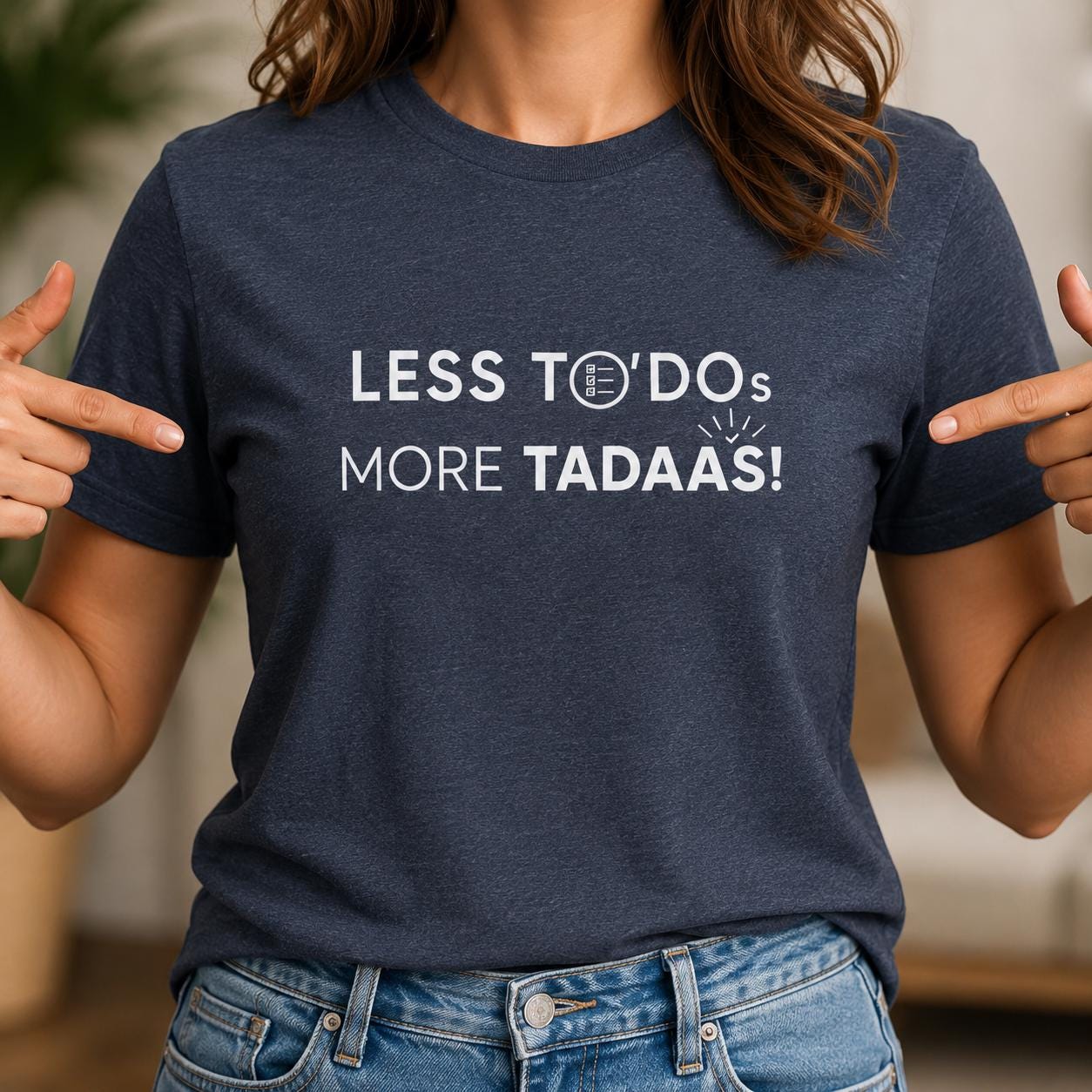 Person trägt dunkelblaues T-Shirt mit weißem Aufdruck 'LESS TO-DOs MORE TADAAS!' und zeigt mit den Fingern darauf