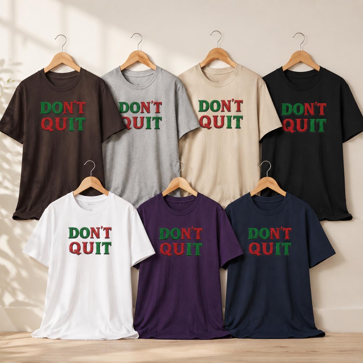 Acht T-Shirts in verschiedenen Farben mit ‚DON’T QUIT‘ Statement auf Holzbügeln an Kleiderstange