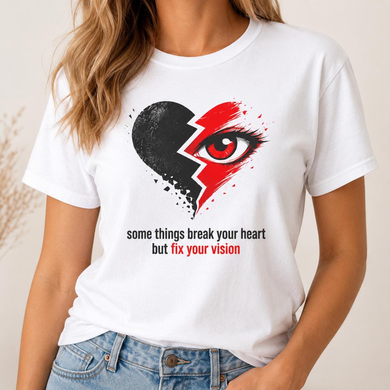 Weißes Unisex T-Shirt mit großem Print eines halbierten gebrochenen Herzens und einem Auge, darunter der Spruch 'some things break your heart but fix your vision'