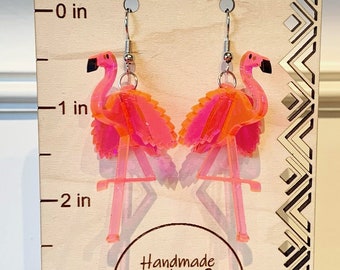 May include: Pink flamingo earrings with silver hooks, displayed on a wooden stand with a ruler measuring up to 3 inches. The stand also has a circular sticker that says "Handmade by Natalie".