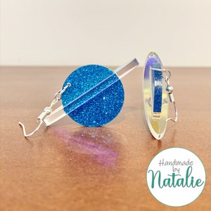 May include: A pair of blue glitter earrings with a silver bar and hook. The earrings are handmade by Natalie.