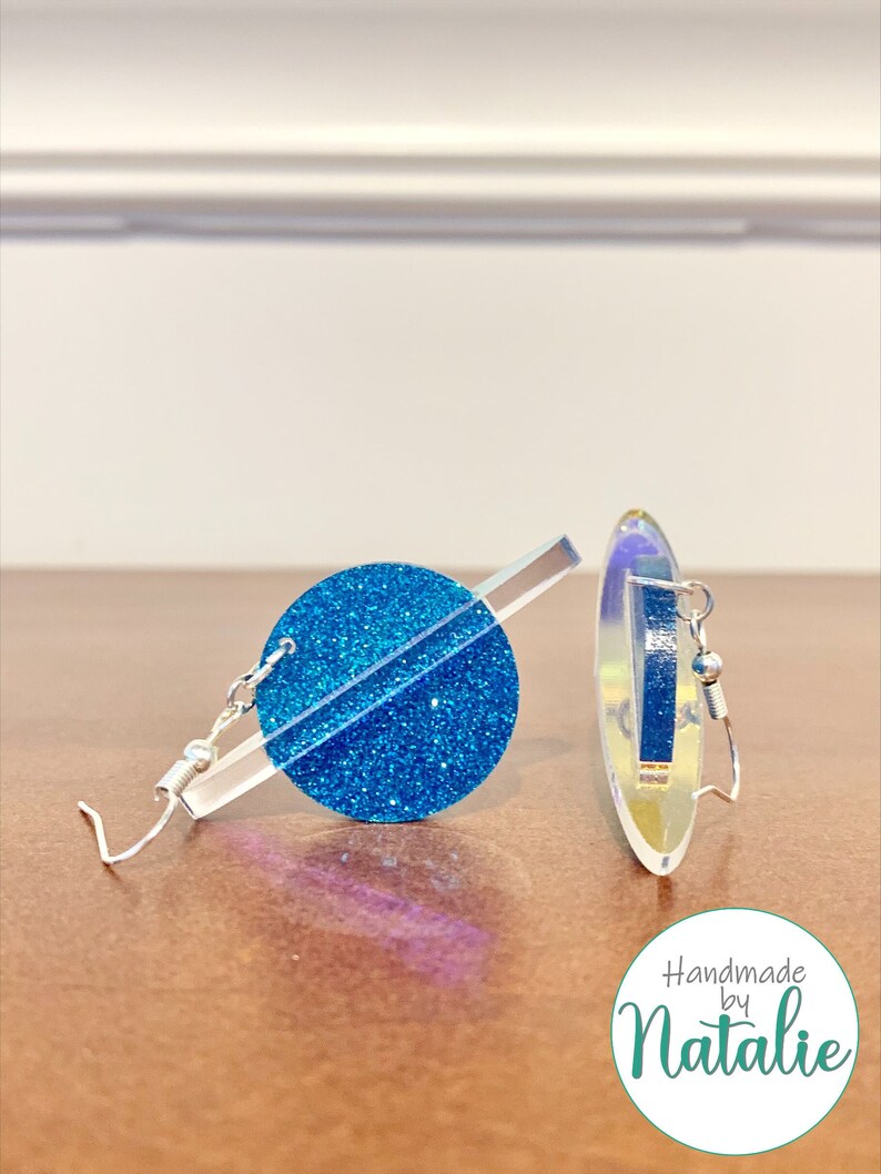May include: A pair of blue glitter earrings with a silver bar and hook. The earrings are handmade by Natalie.