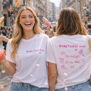 May include: Two women wearing white t-shirts with pink text and holding cocktails. One shirt says "Bride's Final Trip" and the other says "Barcelona 2026". They are in a crowd, celebrating.
