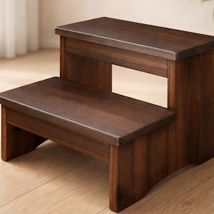 May include: A two-step wooden stool with a rich, dark brown finish. The stool has a rectangular top and a lower step, both with a smooth surface. The design is simple and functional, suitable for various uses around the home.