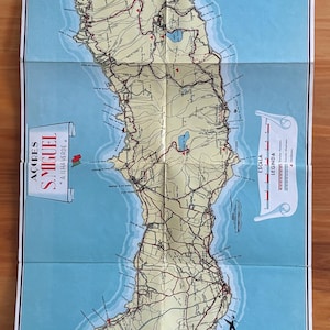 Peut inclure: Carte pliée vintage de l'île de São Miguel aux Açores, Portugal. La carte présente une topographie détaillée, des routes et des noms de lieux, avec une rose des vents et du texte en portugais. La carte est sur fond bleu.