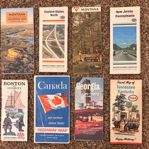 May include: A collection of vintage highway maps from various states and regions, including Montana, Canada, and Georgia. The maps feature colorful illustrations and text, with the AAA logo visible on several.