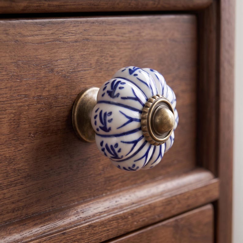 Pu&ograve; includere: Un pomello per cassetto in ceramica scanalata di forma rotonda, caratterizzato da una base bianca con motivi floreali dipinti a mano in blu. Il pomello &egrave; fissato a un cassetto in legno scuro con una base circolare in ottone anticato.