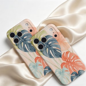 May include: Two smartphone cases featuring a watercolor-style botanical print of monstera leaves in shades of dark teal, soft peach, and pale mint green against a light cream background, with cutouts for the camera lenses and flash.