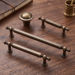 May include: A collection of antique brass hardware including one round cabinet knob and three elongated drawer pulls with hexagonal bars and rounded ends. The metal finish has a darkened, weathered appearance with visible metallic highlights.