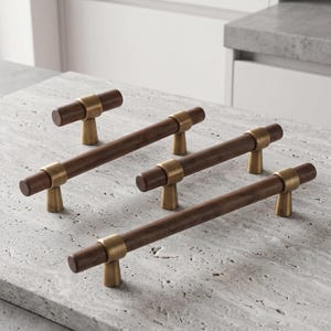 May include: A collection of four cabinet pulls featuring cylindrical dark brown wooden bars accented with brushed brass metal mounts. The set includes one small knob-style pull and three longer bar-style handles with matching hardware.