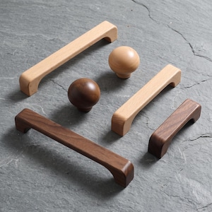 May include: A collection of wooden cabinet hardware including three rectangular drawer pulls and two spherical knobs. The items feature two distinct wood tones, with some pieces in a light natural finish and others in a darker, rich brown wood grain.