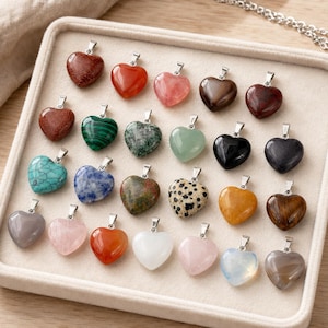 May include: A collection of twenty-five heart-shaped gemstone pendants arranged in a grid. Each pendant features a silver-toned metal bail and is crafted from various polished stones, including turquoise, rose quartz, malachite, and tiger's eye.