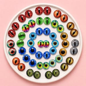 May include: A collection of round glass cabochons featuring various animal eye designs with vertical pupils. The cabochons display a wide spectrum of colors including red, green, blue, yellow, and orange, arranged in a circular pattern on a white tray.