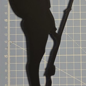 Peut inclure: Silhouette noire d'un soldat en uniforme de la Première Guerre mondiale, tenant un fusil. La silhouette est en position d'attention, avec un sac à dos visible. La base comporte trois trous. L'image est sur une grille bleue.