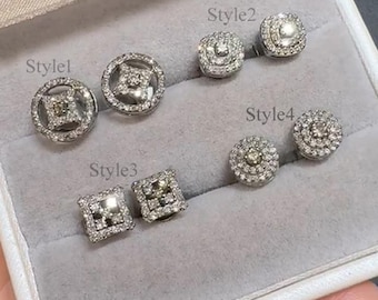 May include: An assortment of four styles of diamond stud earrings. Style 1 features a round design with a central square diamond and a circular frame. Style 2 and 4 are round, while Style 3 is square. All are set in a silver metal.