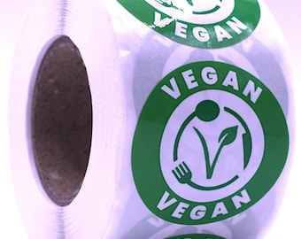 Puede incluir: Un rollo de pegatinas blancas con un diseño circular verde y la palabra "VEGAN" en blanco. El diseño incluye un tenedor, una hoja y un símbolo "V", que indica productos veganos.
