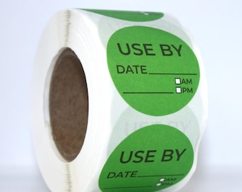 Puede incluir: Un rollo de etiquetas adhesivas circulares de color verde con el texto impreso en negro USE BY, una línea para la fecha y dos pequeñas casillas de verificación marcadas como AM y PM. Las etiquetas están enrolladas en un núcleo de cartón.