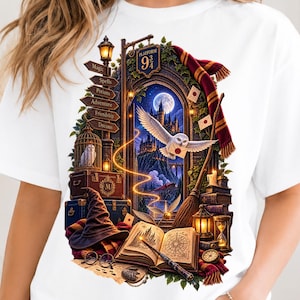 May include: A white t-shirt featuring a detailed graphic of a magical scene with a stone archway, a flying white owl carrying a letter, a castle, a full moon, a signpost labeled Platform 9 3/4, a wizard hat, an open book, and a broomstick.