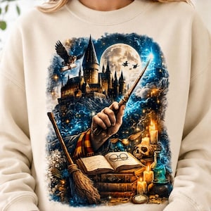Peut inclure: Un sweat-shirt beige à col rond orné d'une impression graphique représentant une main tenant une baguette magique, un château sous une pleine lune, un hibou, un balai, un livre ouvert avec des lunettes, des bougies, un crâne et des fioles.