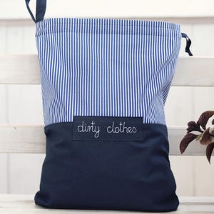 Può includere: Un sacco per la biancheria a righe blu navy e bianche, con una base blu navy tinta unita. Le parole "dirty clothes" sono ricamate in bianco su una toppa blu navy. Chiusura con coulisse.