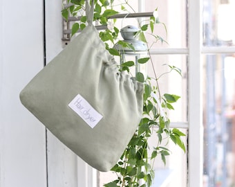 May include: A light green drawstring bag with a white label that says "Hair dryer". The bag is hanging from a hook near a window.