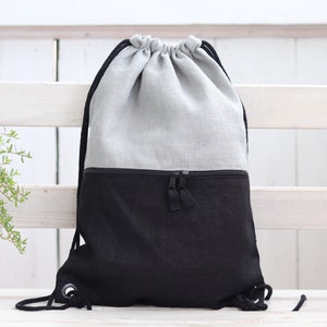 Peut inclure: Un sac à dos en lin gris et noir avec un cordon de serrage. Le sac à dos a une poche zippée à l'avant.