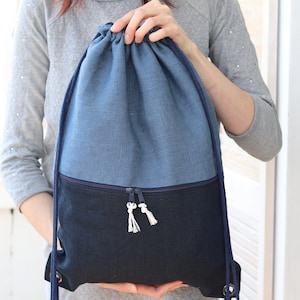 Op de afbeelding: Een blauwe en zwarte trekkoordtas met een ritsvak. De tas is gemaakt van een textuurstof en heeft een wit trekkoord.