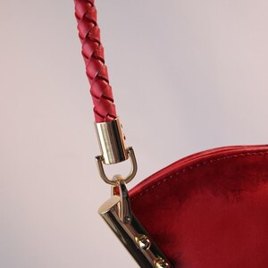 May include: Close-up of a red leather handbag with a braided strap and gold hardware.