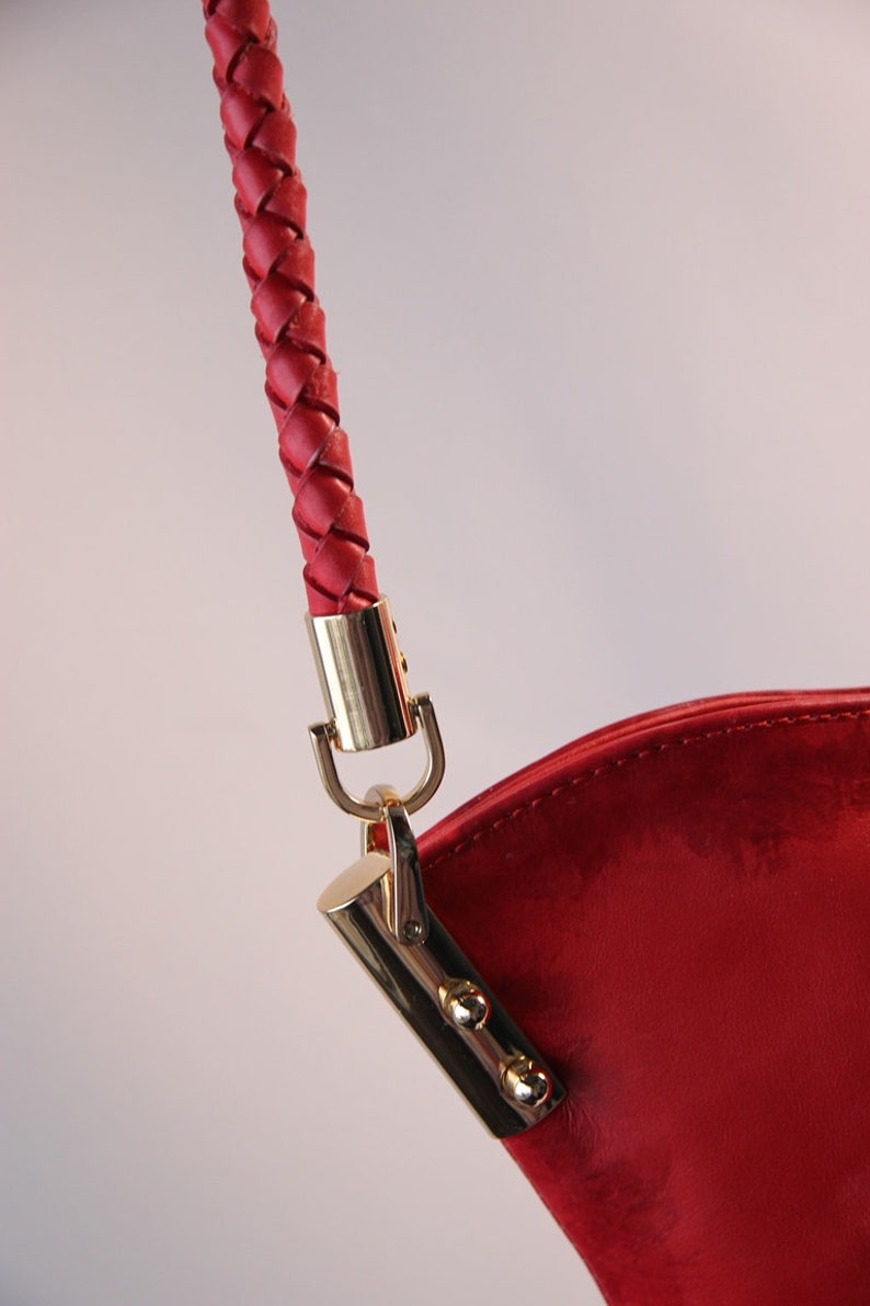 May include: Close-up of a red leather handbag with a braided strap and gold hardware.