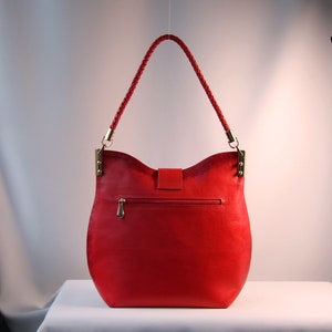 May include: A red leather handbag with a braided strap and gold hardware. The bag has a flap closure and a zippered pocket on the back.