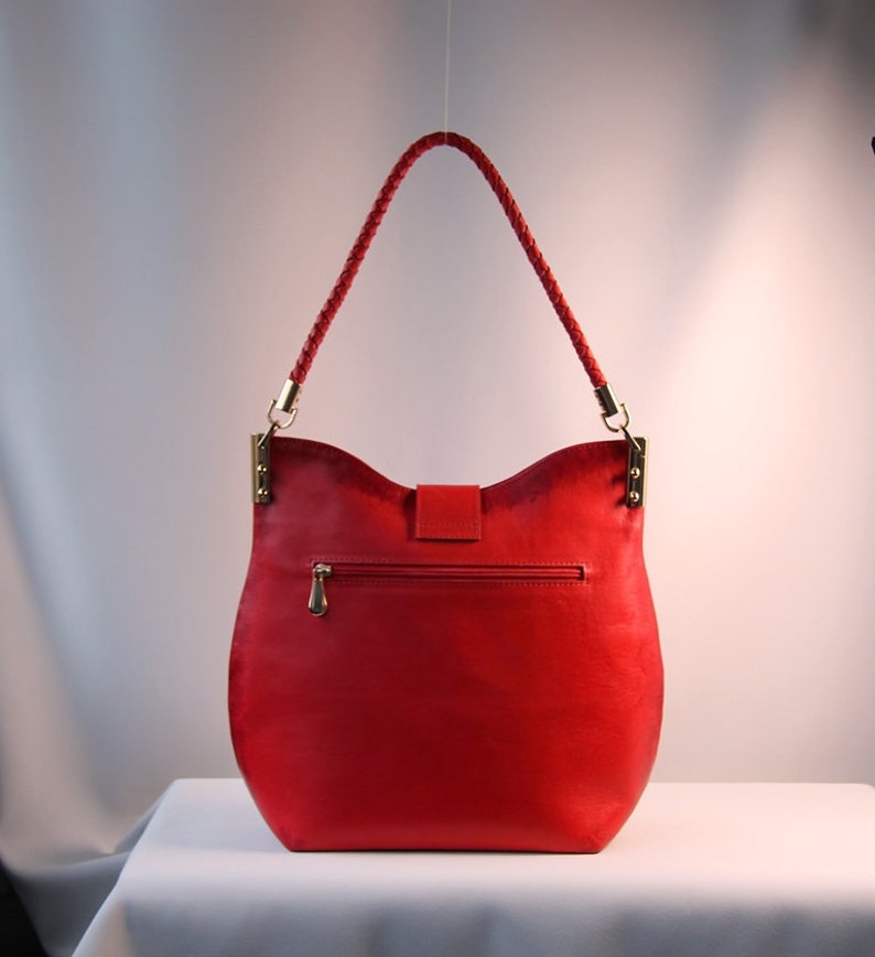 May include: A red leather handbag with a braided strap and gold hardware. The bag has a flap closure and a zippered pocket on the back.