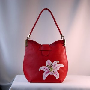 May include: A red leather handbag with a braided strap and a painted lily flower design.