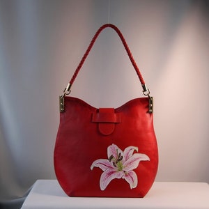 May include: A red leather handbag with a braided strap and a painted lily flower design.