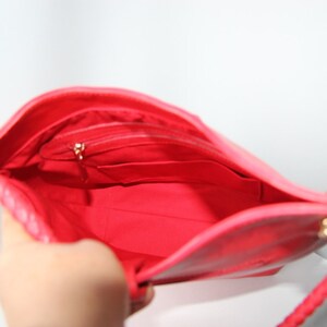 May include: The inside of a bright pink handbag with a gold zipper and a gold chain strap. The bag has a small pocket on the inside.