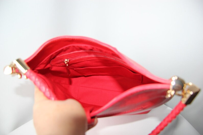 May include: The inside of a bright pink handbag with a gold zipper and a gold chain strap. The bag has a small pocket on the inside.