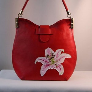 May include: A red leather handbag with a white lily flower design. The bag has a top flap closure and a braided strap.