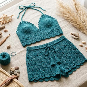 Può includere: Un completo due pezzi all'uncinetto color verde acqua composto da un top corto stile allacciato al collo con bordo smerlato e pantaloncini abbinati con coulisse in vita e nappe. Il completo presenta un motivo a punto conchiglia dettagliato.