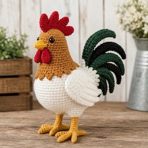 May include: A handcrafted crochet cockerel featuring a tan head and neck, a white body, and yellow feet. The cockerel has a bright red comb and wattle, a yellow beak, black eyes, and a tail composed of layered dark green and black crochet feathers.