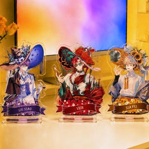 May include: Three clear acrylic character standees featuring anime-style figures. The left figure wears a blue hat and is labelled Liu Xiao. The centre figure wears a red hat and is labelled Vein. The right figure wears a straw hat and is labelled Xia Fei.
