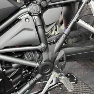 Peut inclure: Un cadre de moto noir mat doté d'une structure en acier tubulaire, d'un logo GS bien visible sur le carter latéral, de tringleries mécaniques apparentes, d'un repose-pied texturé et d'un support en métal argenté, avec le texte Cyril M.