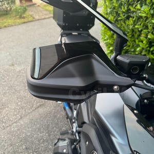 May include: Close-up of a black motorcycle with a silver and black side mirror. The mirror has the text "BMW Motorrad" on it. The motorcycle has a black handlebar guard and a blue and white BMW logo.