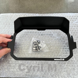 Op de afbeelding: Een zwarte motorfiets koplampkuip met de tekst "R1250GS" aan de zijkant. De kuip wordt boven een doorzichtig, met bubbels verpakt oppervlak gehouden. Een klein zakje met hardware is zichtbaar in de kuip.