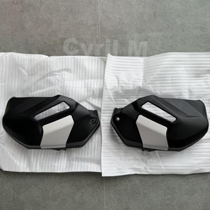 Peut inclure: Une paire de protège-mains de moto noir mat avec un panneau d'accent gris clair et une découpe rectangulaire. Chaque protection présente une forme incurvée et aérodynamique avec un trou de montage circulaire sur le bord extérieur.